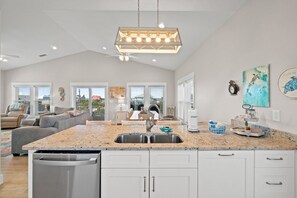 A spacious kitchen with a granite countertop, stainless steel sink, and white cabinetry. There is a dining area with a table and chairs, and a ceiling fan.