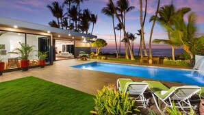 A modern house with a swimming pool, outdoor furniture, and palm trees. - Malulani Villa, Luxury Oceanfront 3 BR, Private Pool, Hot Tub & Pickleball! (Kamuela)
