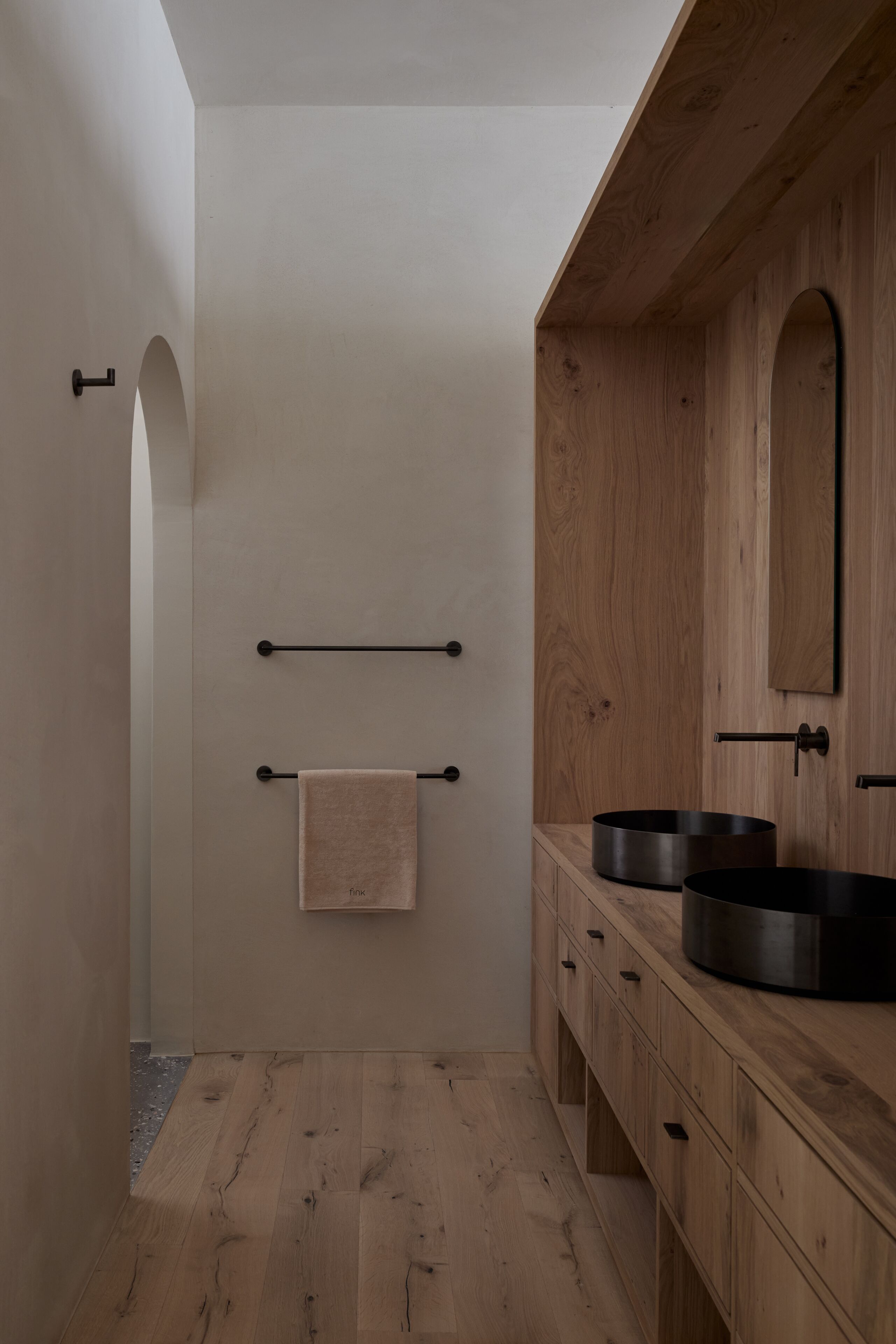 Une salle de bain moderne avec des meubles en bois, un grand miroir et deux lavabos noirs.