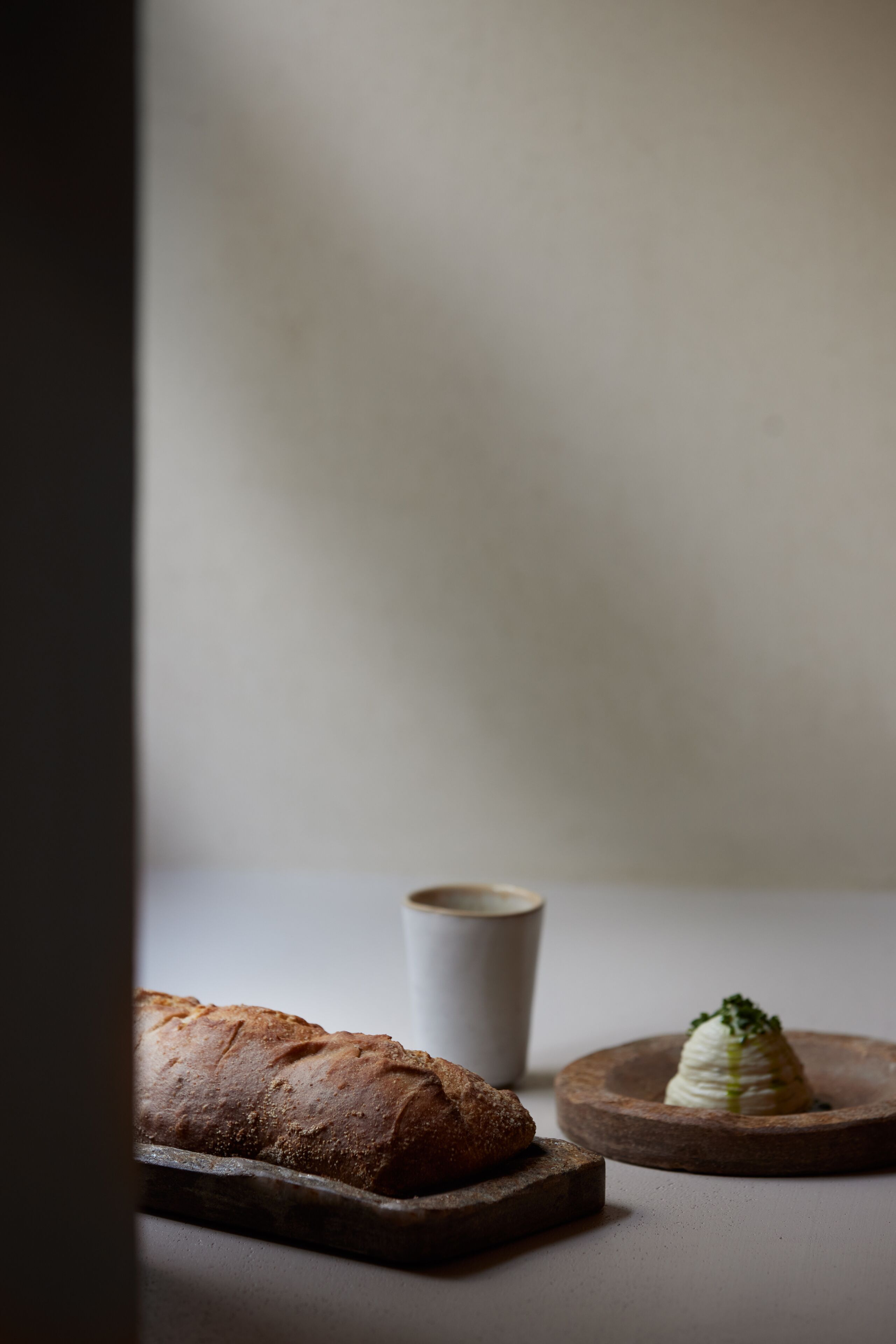 Ein Brotlaib auf einem Holzboden, eine kleine Tasse und ein Teller mit einer Speise.