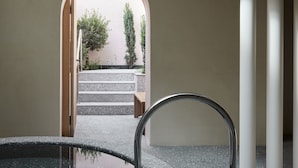 Un baño moderno con una bañera independiente, un tragaluz circular y vistas de un jardín exterior a través de un arco.