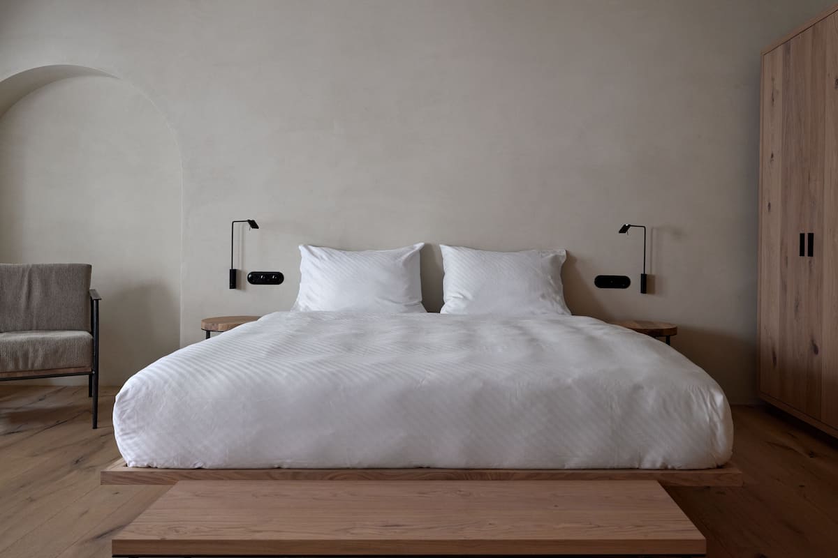 A minimalist bedroom with a large bed, two bedside tables, a chair, and a wardrobe.