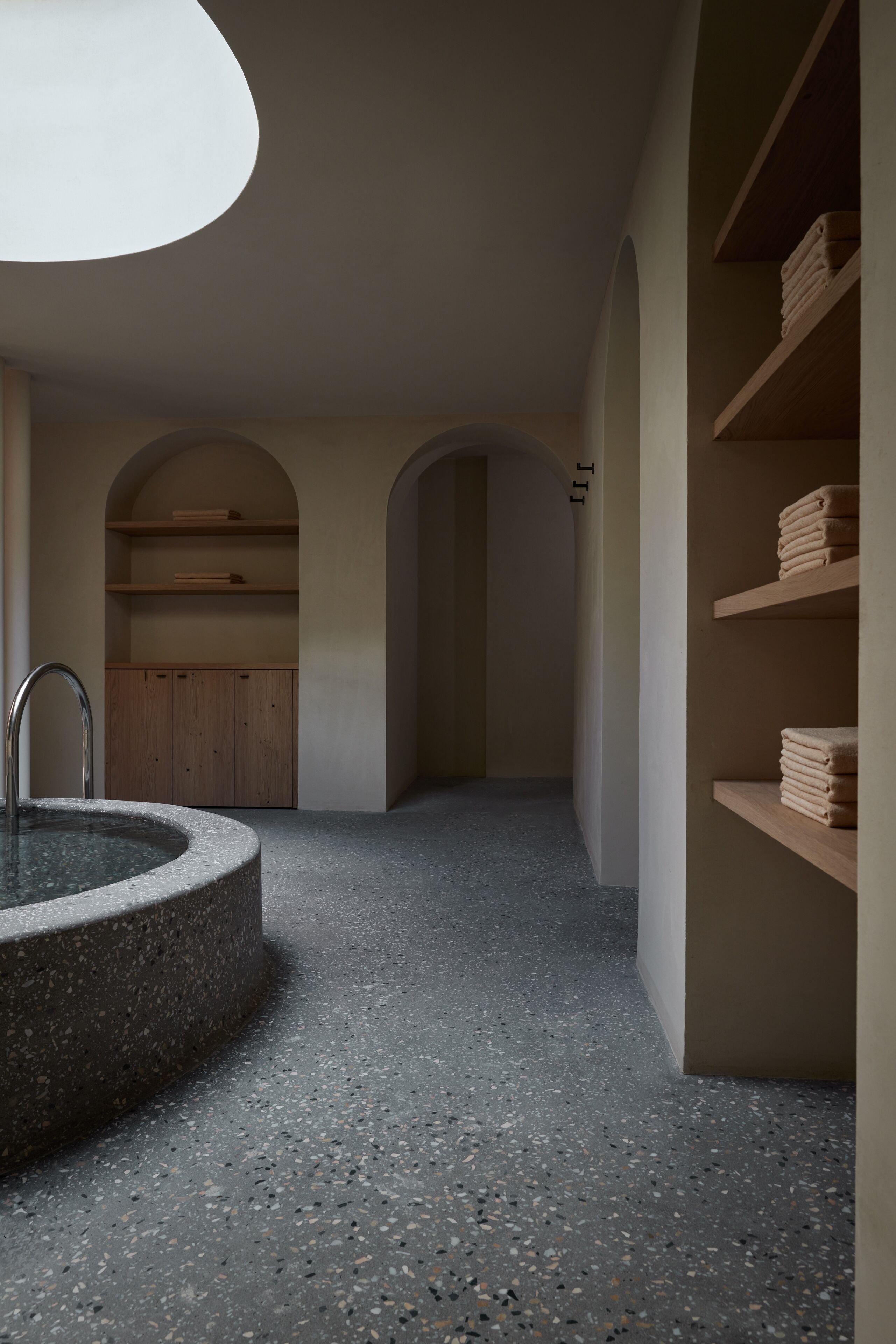 Un espacio de spa con una bañera de piedra circular, estantes de madera e iluminación en el techo.
