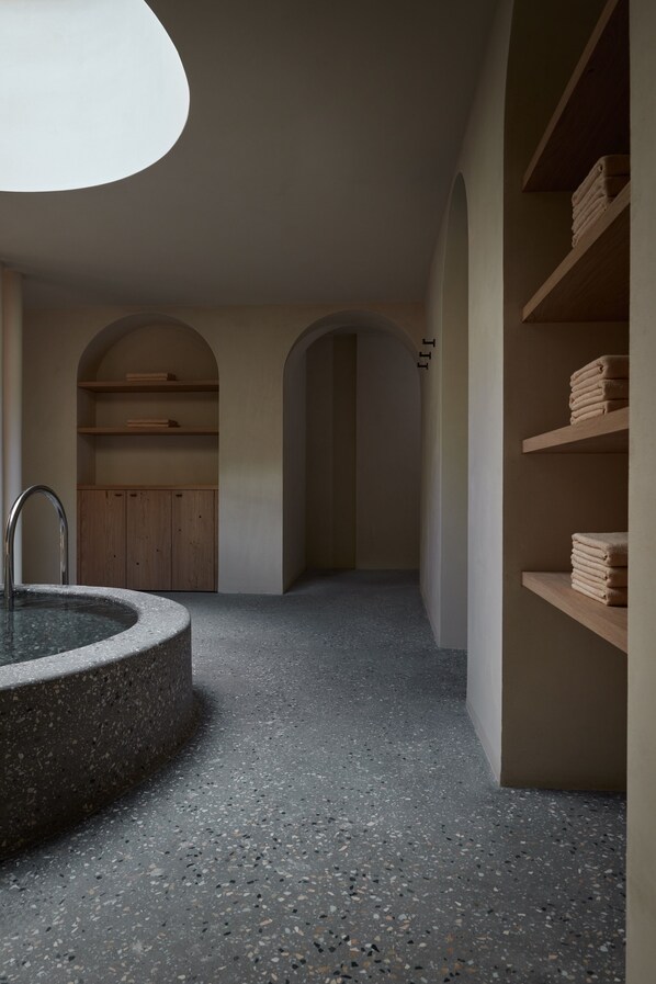 A spa area with a circular stone bathtub, wooden shelves, and a ceiling light. - fink Restaurant & Suites (Bressanone)