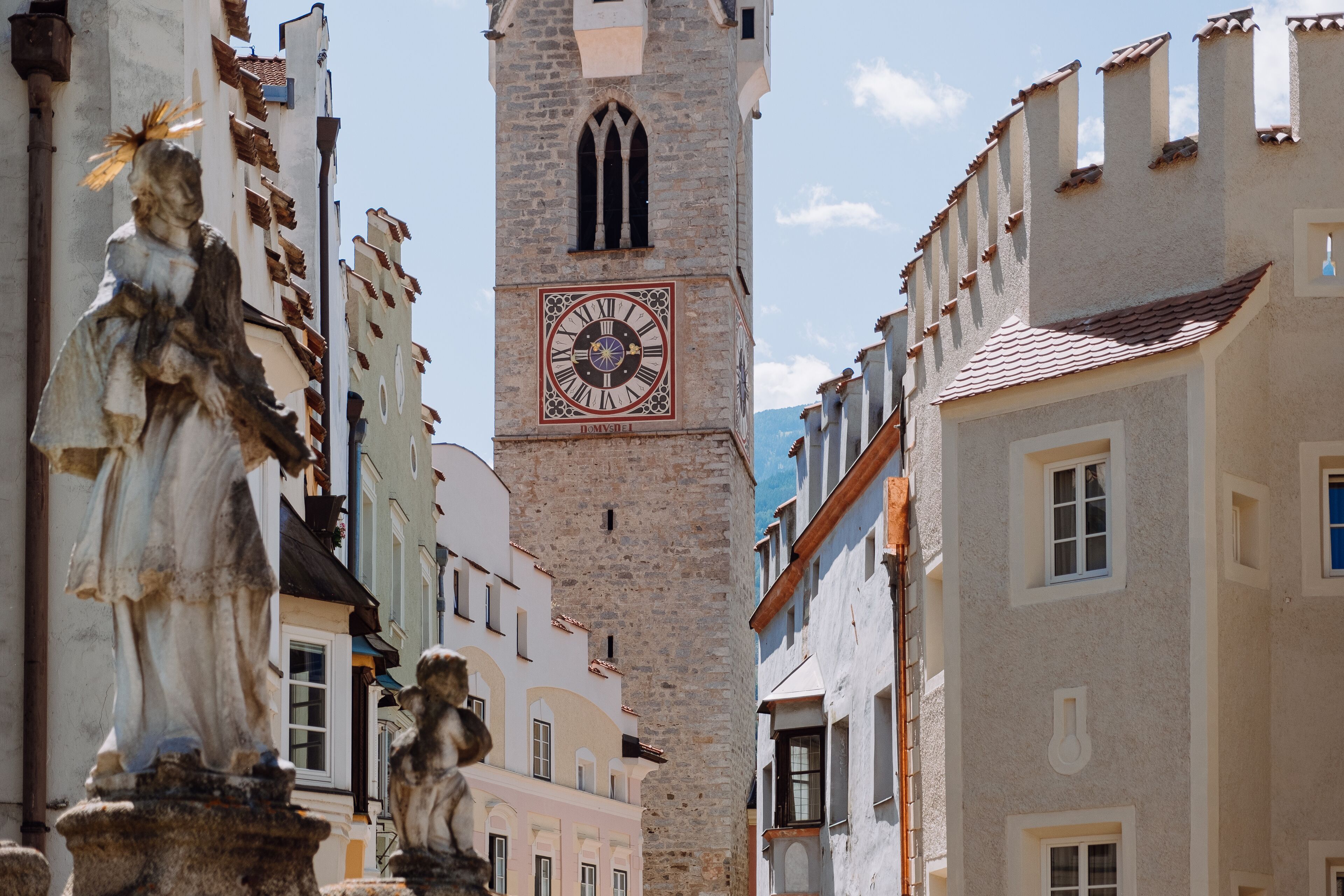 Uma torre histórica com relógio, ladeada por edifícios com arquitetura tradicional.