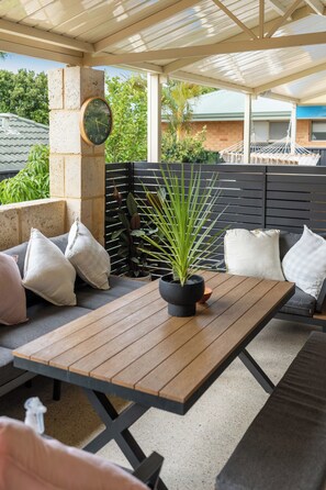 An outdoor seating area with a wooden table, cushions, and a potted plant. - 5BR and pool luxury home (Kinross)