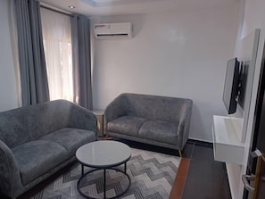 A modern living room with two grey sofas, a small round table, and a TV mounted on the wall. - Hotel Thirty Five (Lagos)