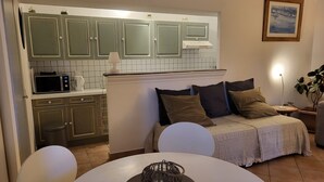 A compact kitchen with a microwave, kettle, and cabinets. There is a dining area with a table and chairs, and a bed with pillows.