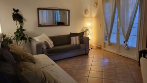 A living room with a sofa, a plant, a mirror, a fan, and a window with curtains.