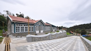 A building with a red-tiled roof, stone walls, and a paved walkway leading to a gated entrance. - The Hearth (Kodaikanal)