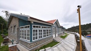 A two-story building with a stone facade and blue trim, featuring large windows and a red-tiled roof. - The Hearth (Kodaikanal)
