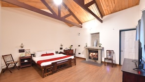 A bedroom with a wooden bed, a fireplace, a television, and a desk. - The Hearth (Kodaikanal)