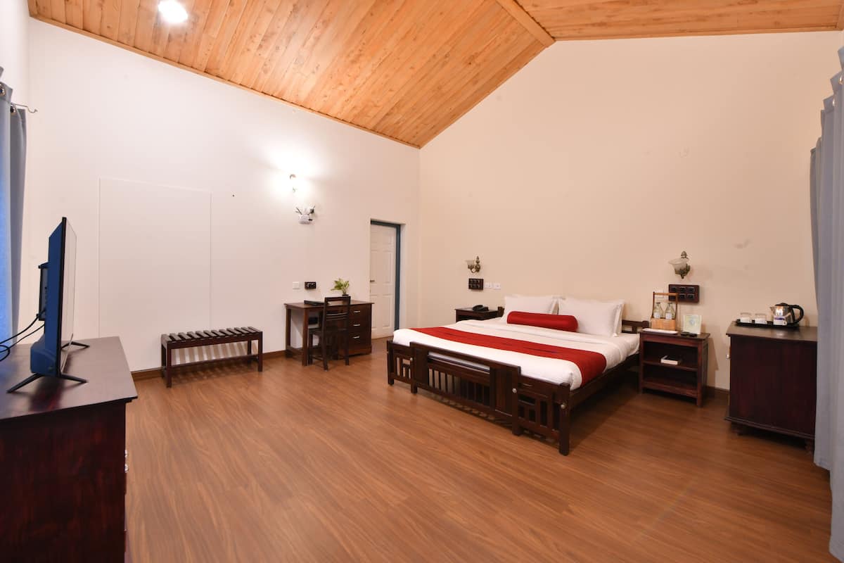 Un dormitorio con techo de madera, cama con colcha roja y blanca, escritorio con computadora y mesita de noche con lámpara.