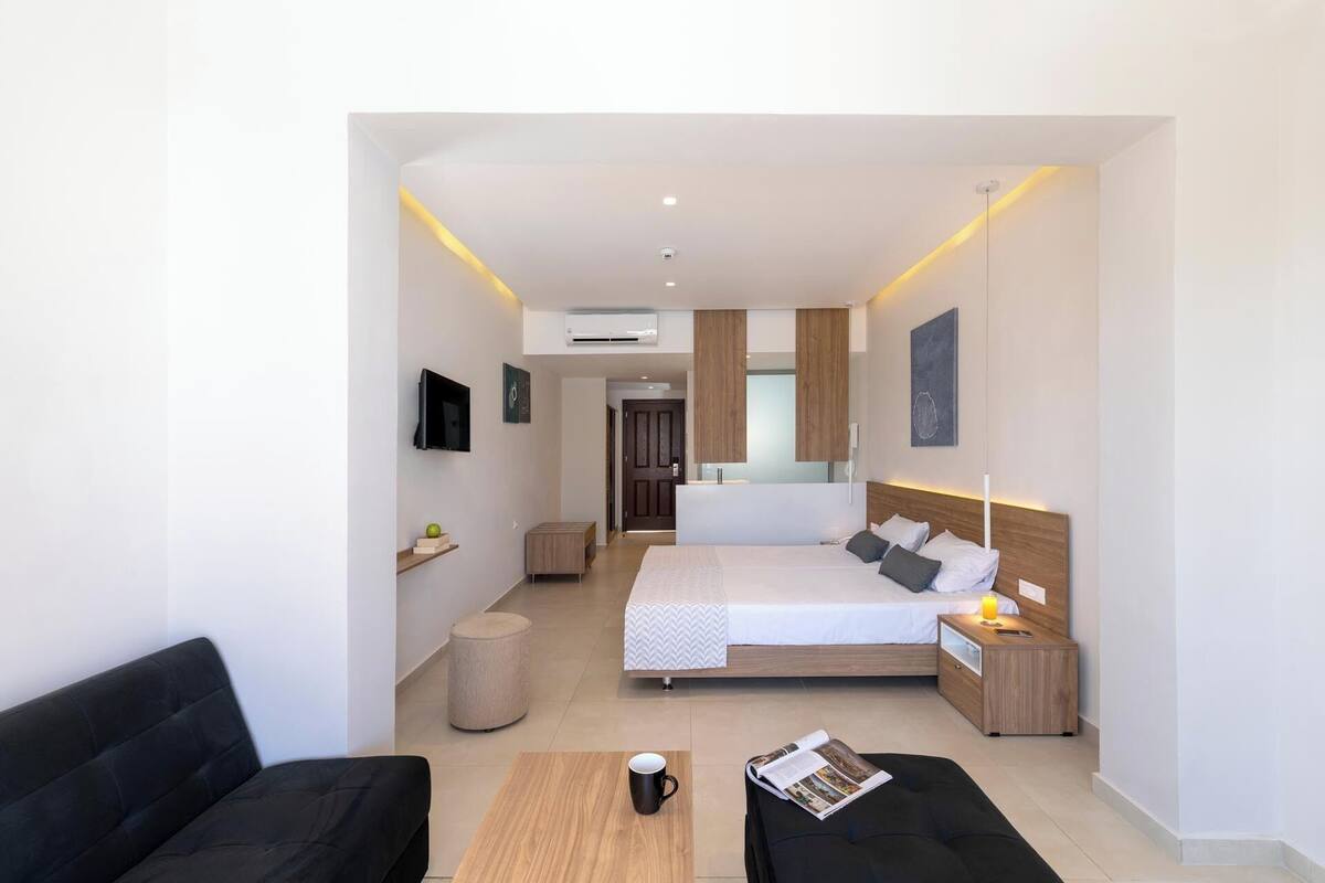 Une chambre d’hôtel moderne dotée d’un grand lit, d’une table de chevet avec une lampe, d’un petit coin salon avec un canapé et d’une table basse.
