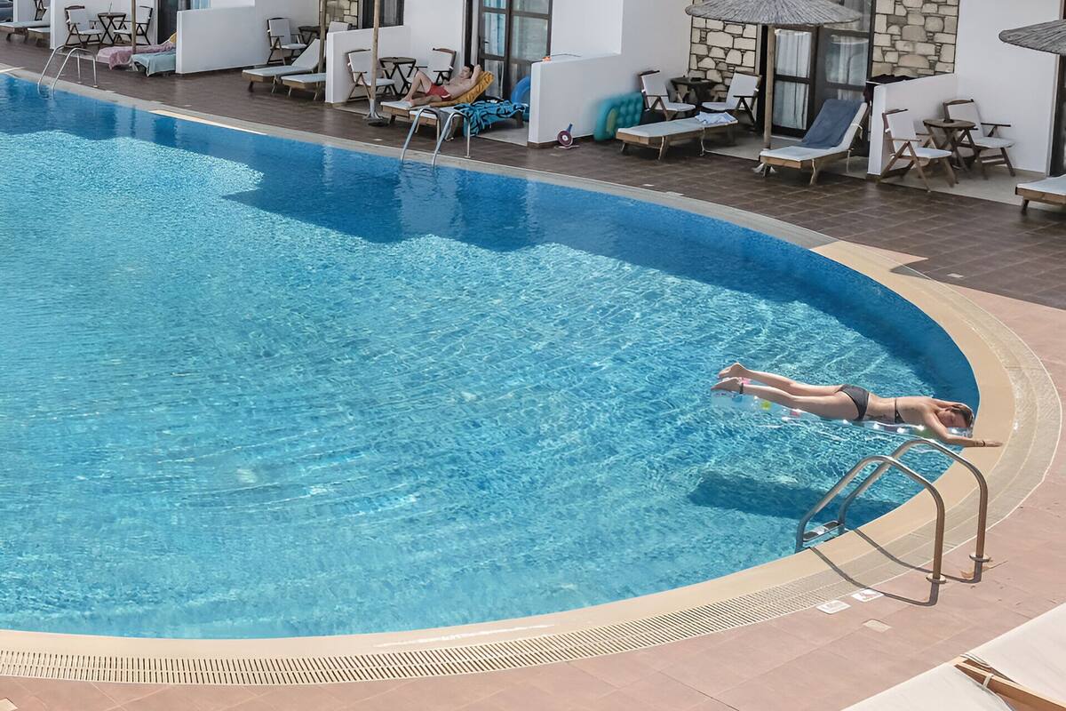 Une piscine entourée de bâtiments à plusieurs étages dotés de balcons, avec des chaises longues et des parasols à proximité.