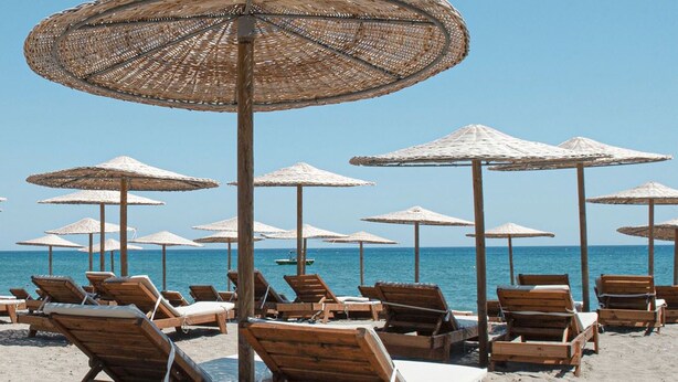 Een strand met houten ligbedden en rieten parasols.