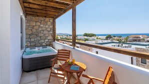 Een balkon met een stenen muur, houten plafond en een jacuzzi. Er staat een tafel met stoelen en een glas sinaasappelsap.