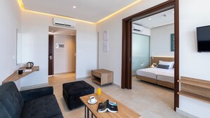 Een moderne hotelkamer met een bank, een tafel met een koffiekopje en schoenen, een bed met een televisie, en een houten bijzettafeltje.