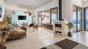Een ruime woonkamer met een open haard, een grote televisie en uitzicht op zee.