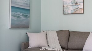 Et værelse med en grå sofa, to puder og et indrammet maleri af et landskab.