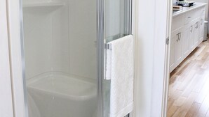 Et moderne badeværelse med brusekabine i glas, et hvidt håndklæde hængende på døren og trægulv.