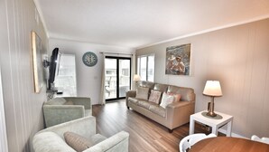 Uma sala de estar com sofá, poltronas, mesa, luminária e um quadro na parede.