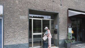 Entrada de un edificio con puerta de vidrio, planta en maceta y un cartel.