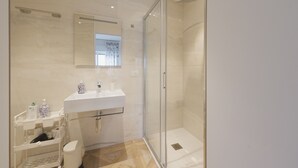 Un baño moderno con cabina de ducha de vidrio, un lavabo blanco y un mueble de tocador con espacio de almacenamiento.