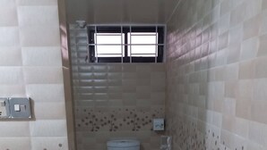 A small, tiled bathroom with a toilet, a hand dryer, and a window above the toilet. - Kishoreganj Resort (Kishoreganj Sadar)
