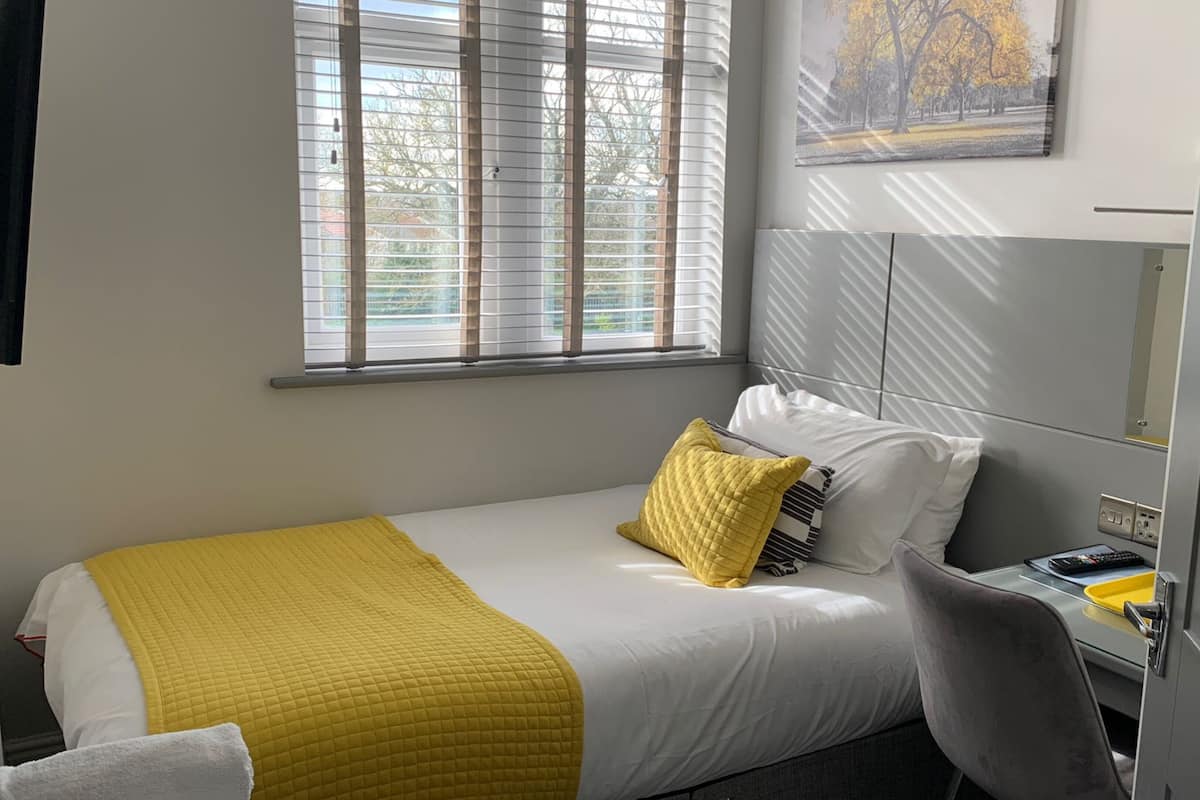 A neatly arranged bedroom with a bed, a bedside table, a chair, and a window with blinds.