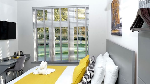 Habitación de hotel con cama, escritorio, silla, televisor de pantalla plana y ventana con persianas.
