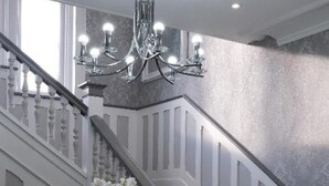 Una gran escalera con balaustres blancos, peldaños cubiertos de alfombra oscura y un candelabro.