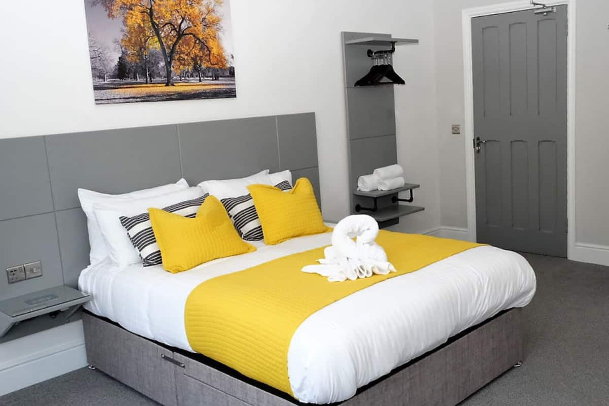 A hotel room with a large bed, a bedside table, a towel rack, and a door.
