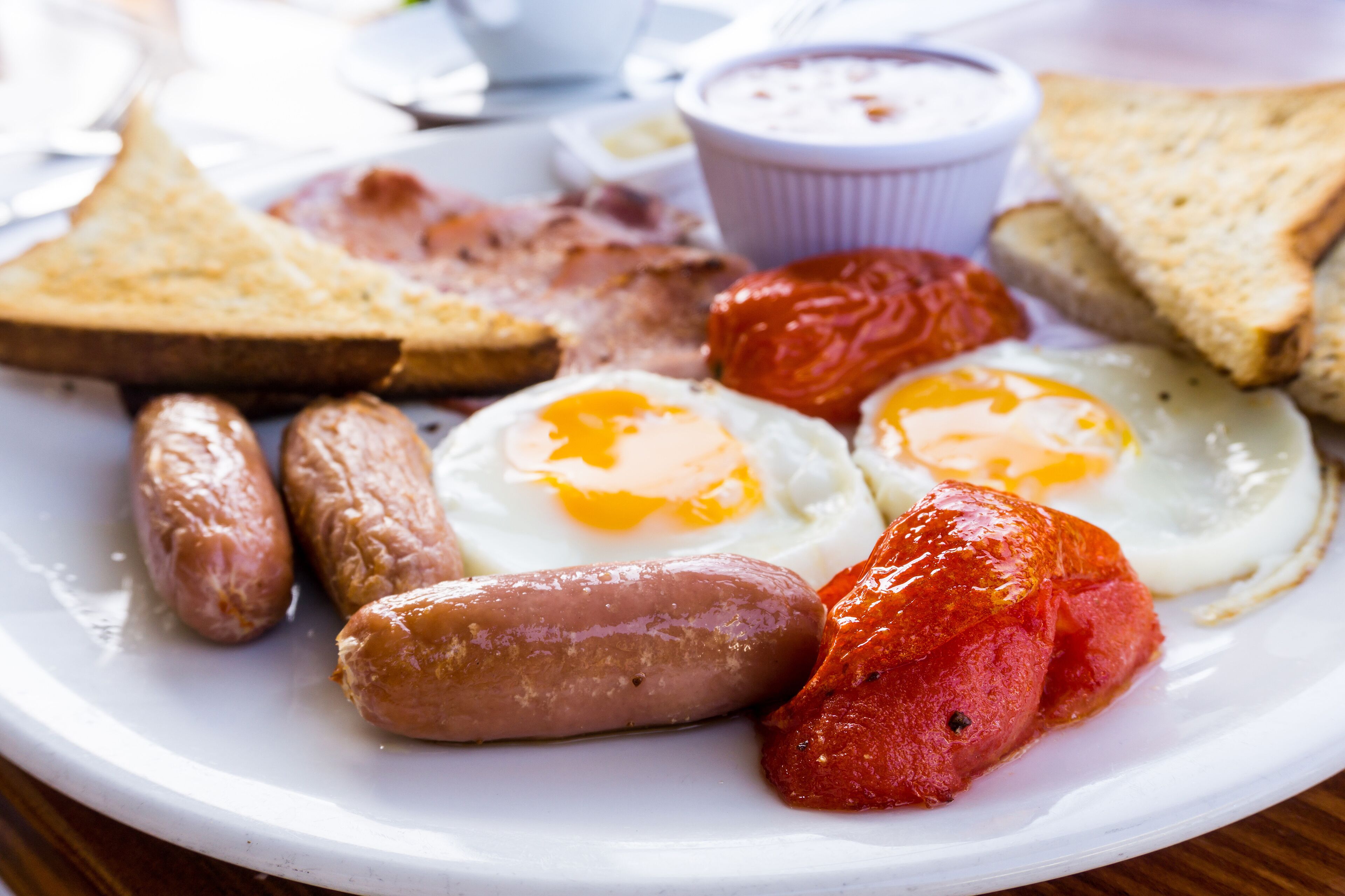 Une assiette de nourriture pour le petit-déjeuner comprenant des saucisses, des œufs et des toasts.