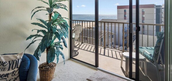 A balcony with a view of the sea, a potted plant, and a chair.