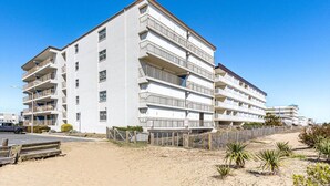 A multi-story hotel with balconies, located near a sandy beach.