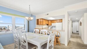 A modern kitchen with wooden cabinets, a white refrigerator, and a dining area with a white table and chairs.