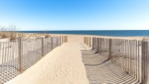 A sandy beach path with wooden fencing on both sides leading to the sea.