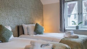 A hotel room with two beds, a patterned wallpaper on one wall, a window with curtains, and a hanging light fixture.