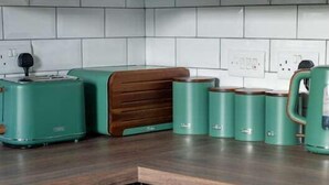 A kitchen with dark cabinets, white tiles, a wooden countertop, a green toaster, and a green kettle.