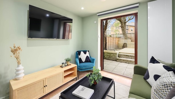 A modern living room with a flat-screen TV, a wooden console table, a blue armchair, and a green sofa. - Classy&Stylish 2 bed flat (London)
