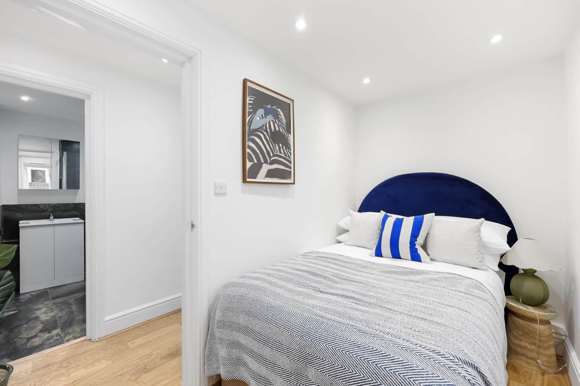 A bedroom with a bed, a nightstand, a lamp, and a painting on the wall.