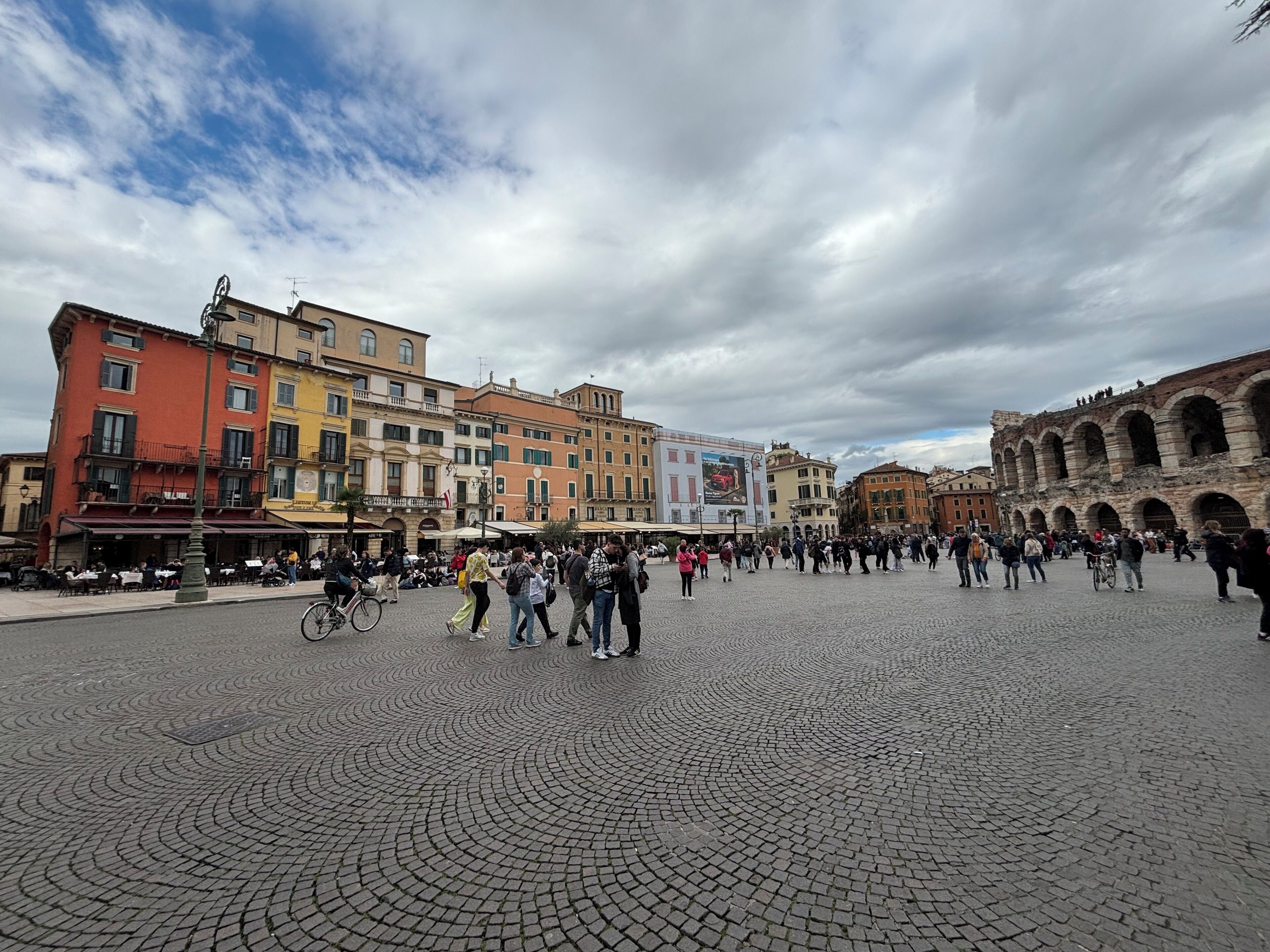 A cobblestone square with historic buildings, a prominent archway, and outdoor seating areas.
