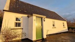 A single-story house with a green door, numbered 10, and a chimney. - Traditional Holiday Cottage Louisburgh. (Louisburgh)