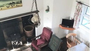 A cozy living room with a fireplace, a television on a shelf, and a dining area with a table and chairs. - Traditional Holiday Cottage Louisburgh. (Louisburgh)