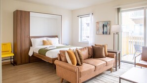 Et hotelværelse med seng, sofa, stol, skrivebord og et vindue med udsigt til bygninger.