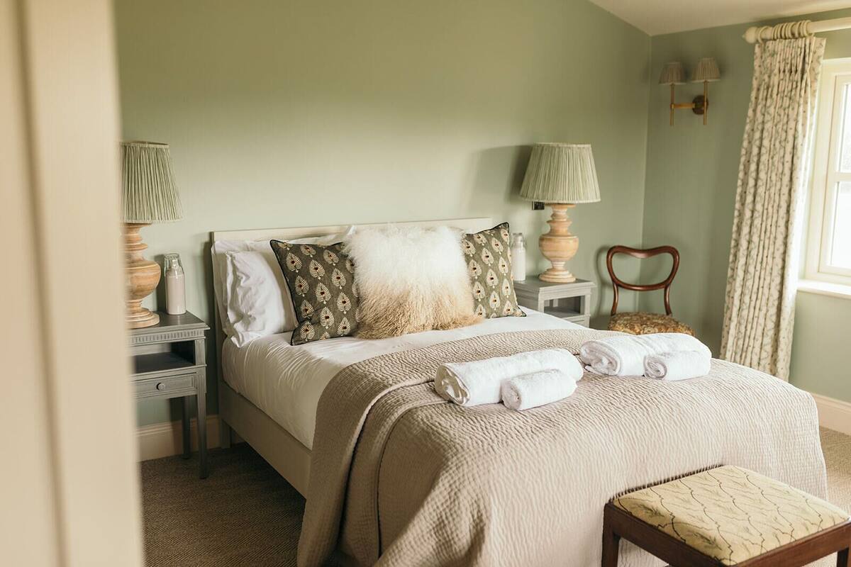A neatly made bed with a white comforter, two pillows, and a folded towel on a wooden bench.