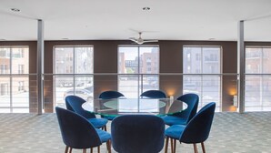 Une pièce moderne avec une table en verre entourée de chaises bleues, de grandes fenêtres donnant sur la ville et un ventilateur de plafond.