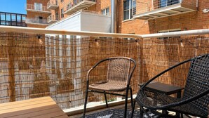 Un balcon agrémenté de meubles en osier, d’une table en bois et offrant une vue sur les bâtiments voisins.