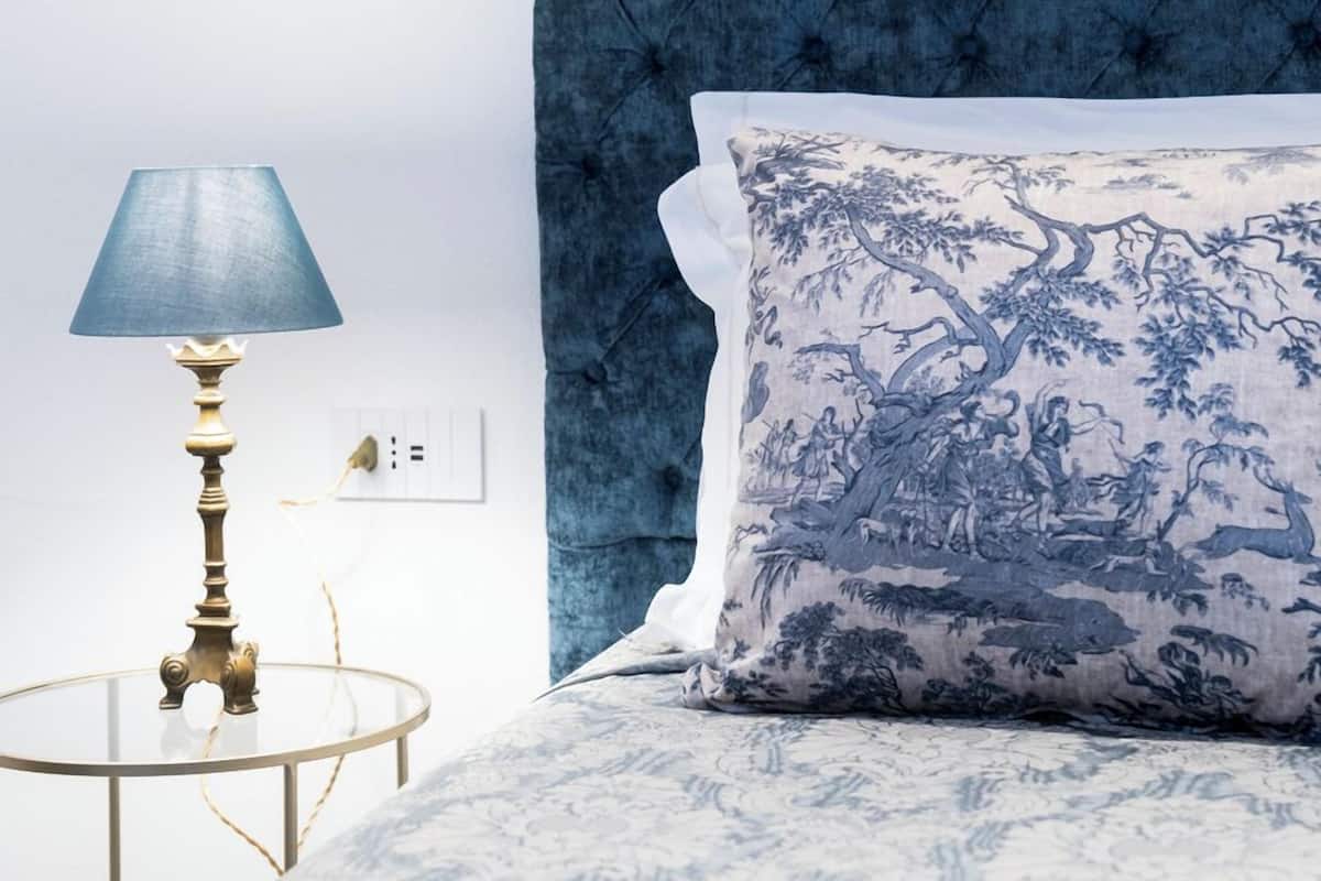 A bedroom with a tufted headboard, a round table with a lamp, and a patterned pillow.